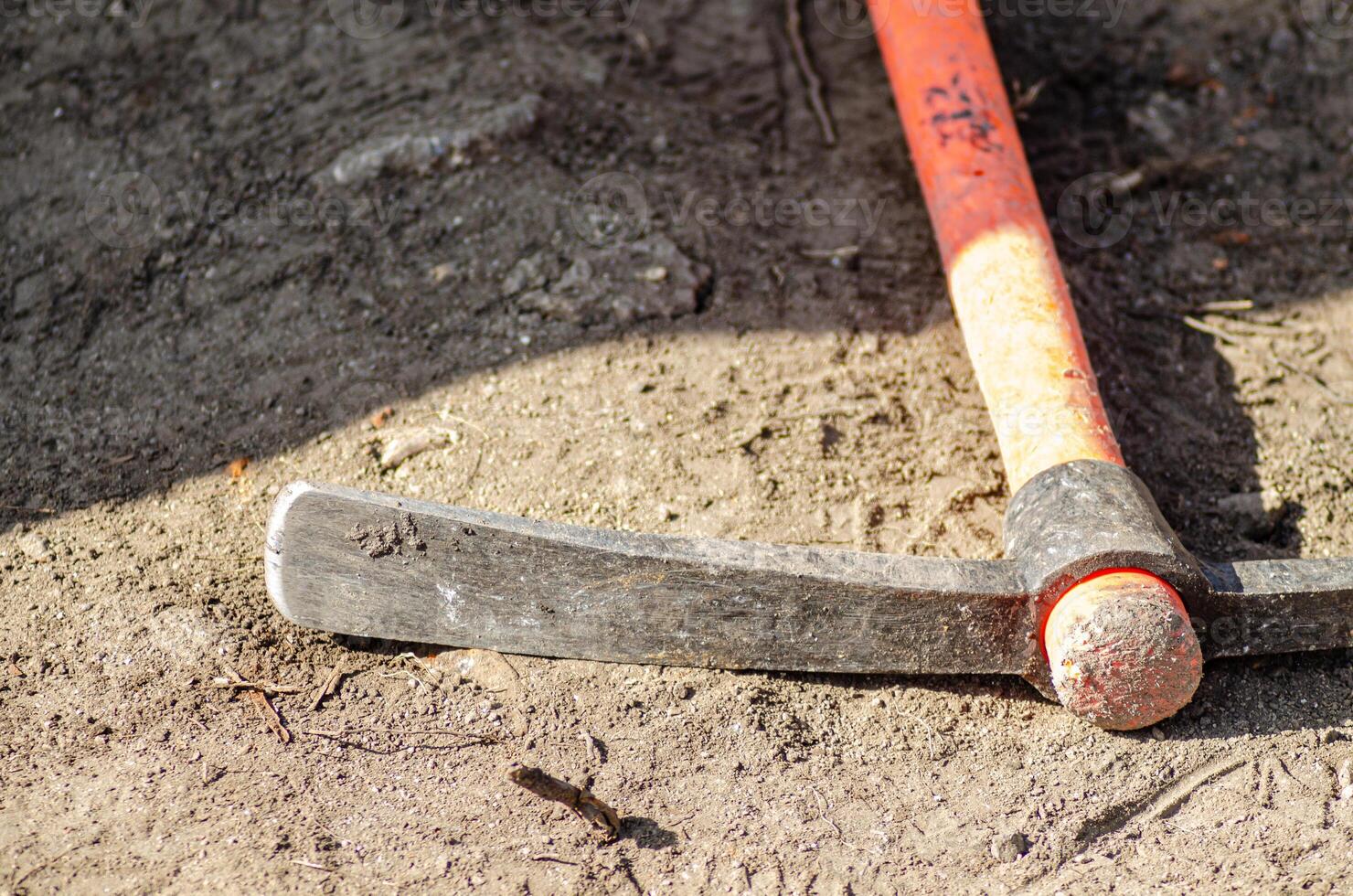 close-up of a pickaxe lying on the ground at a work site, featuring a red Kevlar handle. photo