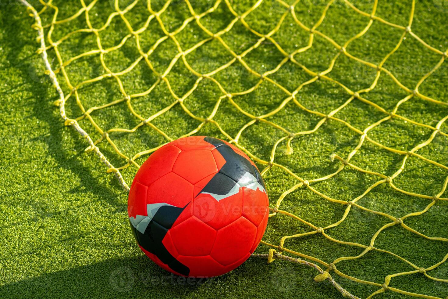 red soccer ball on the net of a goal in a football field photo