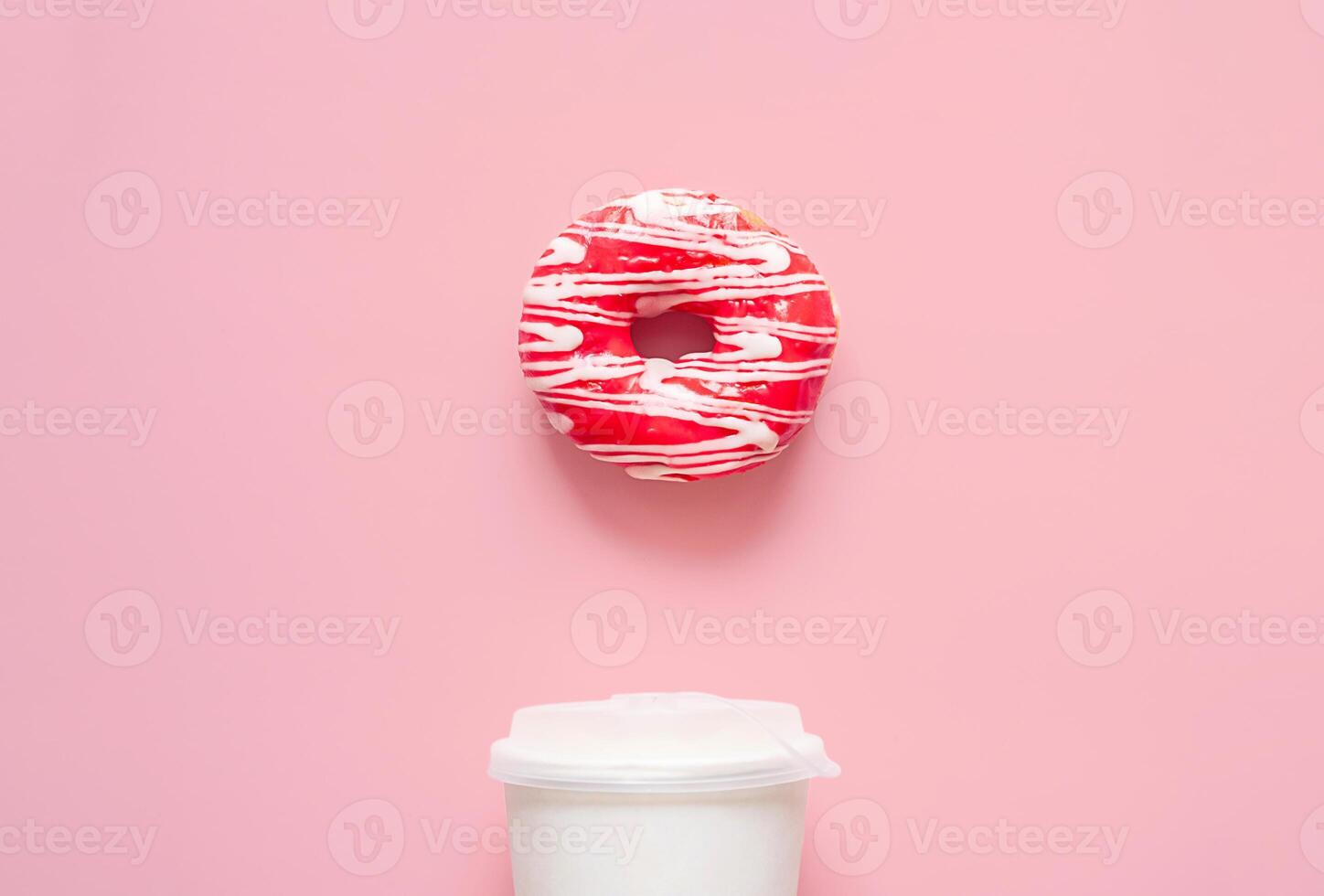 Pink frosted donut with white drizzle and white to go coffee cup. Breakfast or snack time concepts. photo