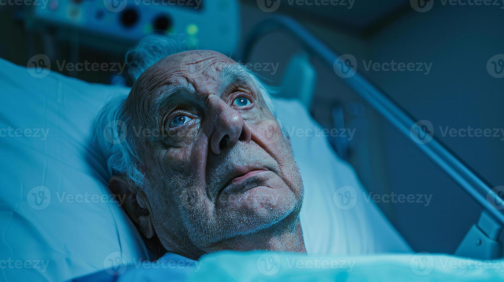 Elderly man in hospital bed looking anxious under blue light photo