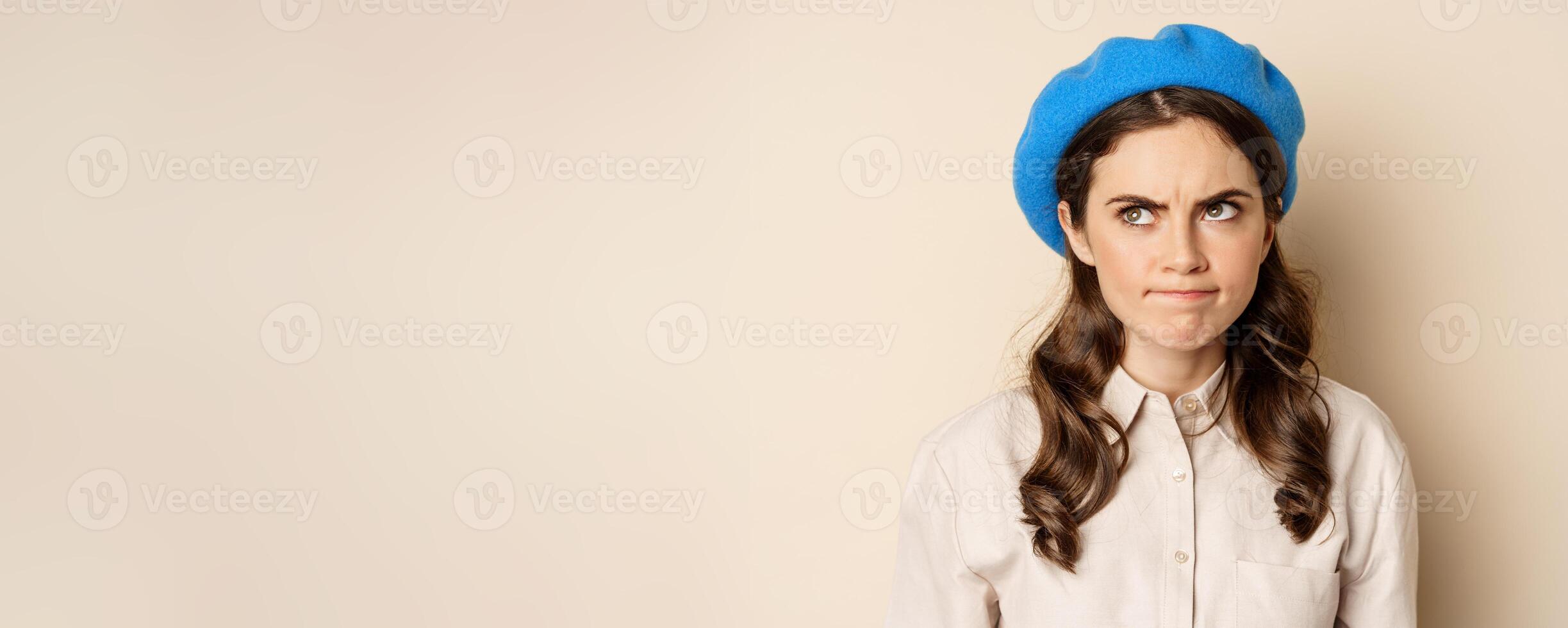 Close up portrait of young beautiful woman sulking, looking angry and disappointed, grimacing displeased, standing over beige background photo