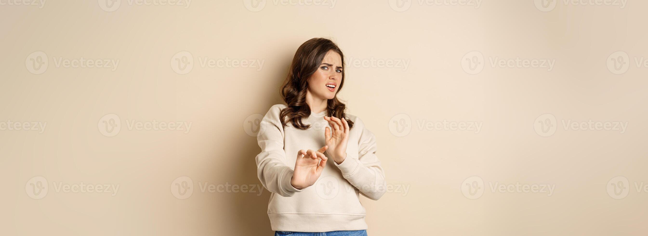No thanks. Woman feeling dislike and rejecting smth disgusting, step back and shake hands to decline offer, standing over beige background photo