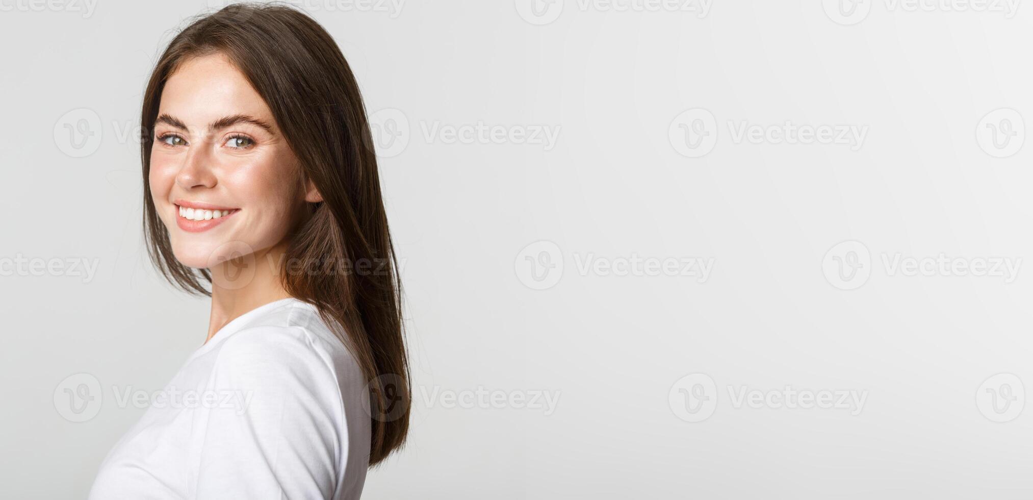Portrait of confident beautiful brunette woman turning face at camera with dreamy look, smiling over white background photo