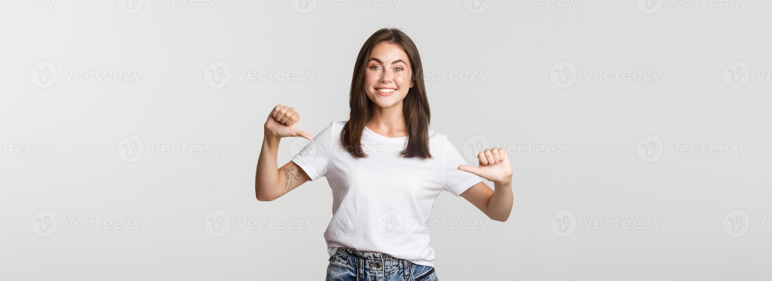 Excited happy brunette girl smiling, pointing fingers at your logo, showing banner photo