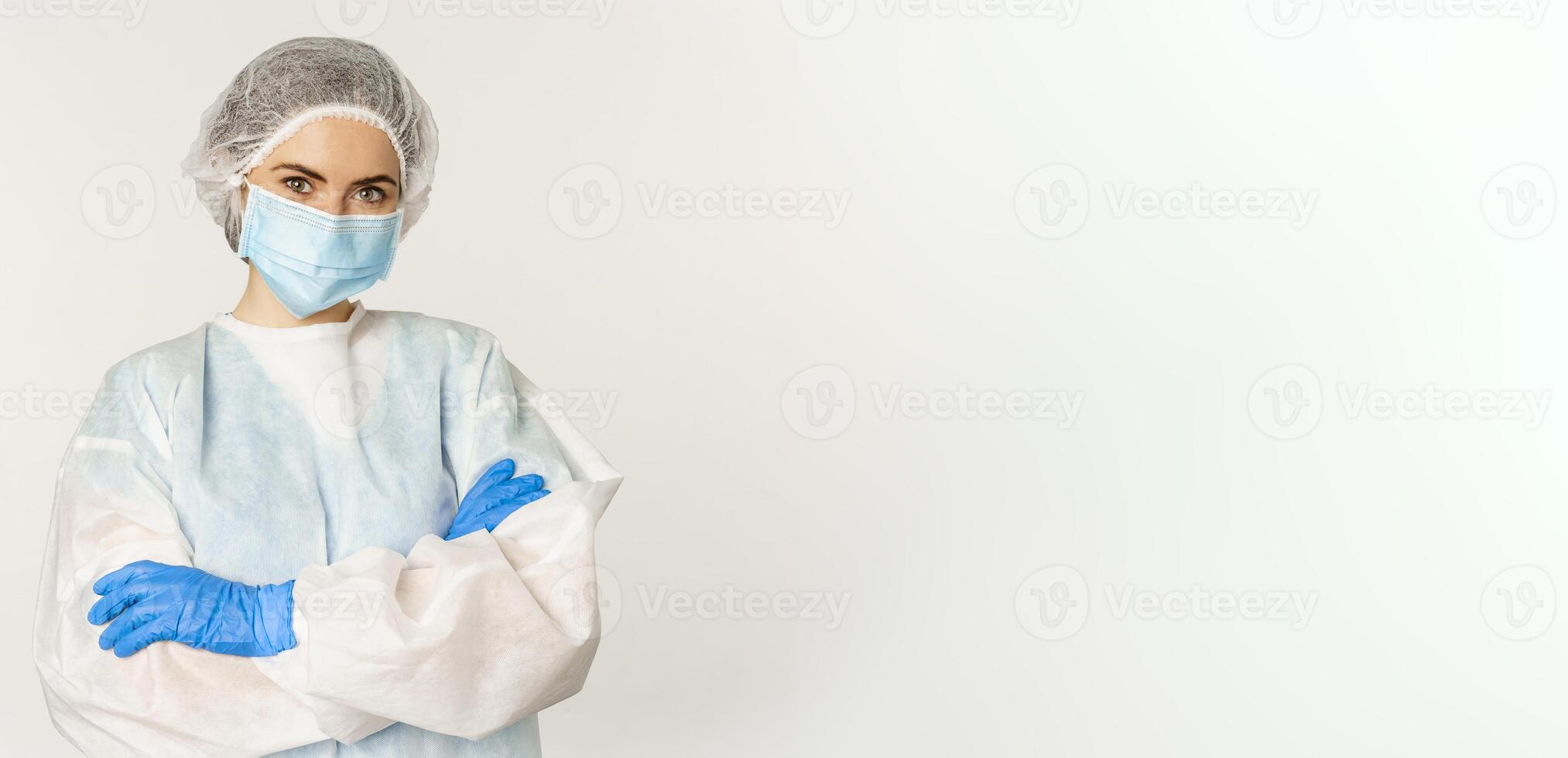 Portrait of doctor, female nurse in personal protective equipment, looking confident and professional, standing over white background photo