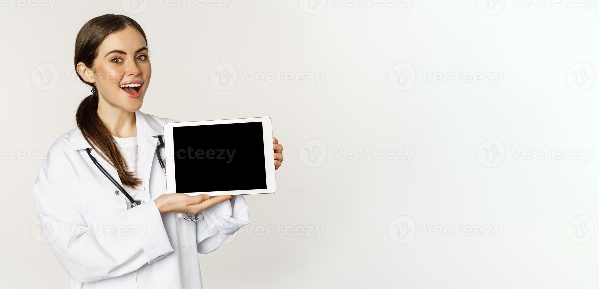 Online medical help, remote appointment. Smiling beautiful woman doctor showing digital tablet screen, demonstrating website logo, standing over white background photo
