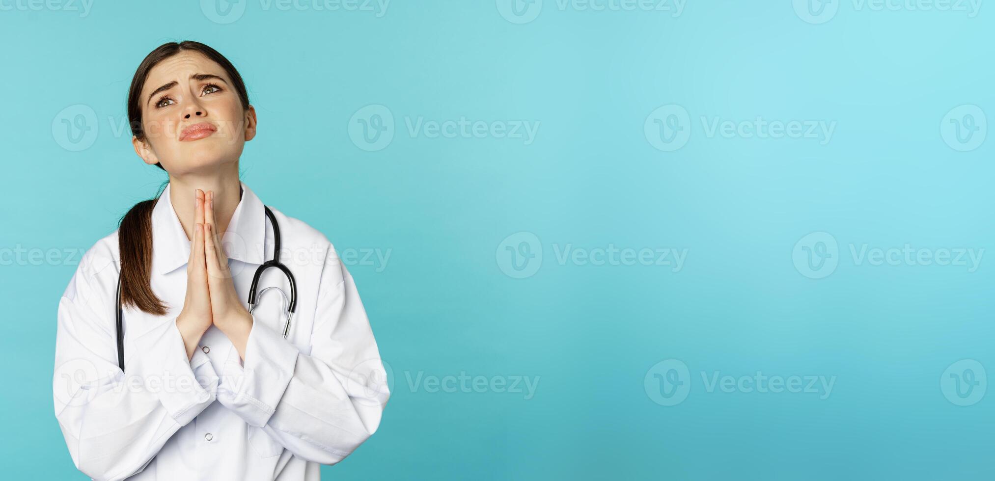 Woman doctor begging, pleading or supplicating, making wish, asking for help, standing desperate against torquoise background photo