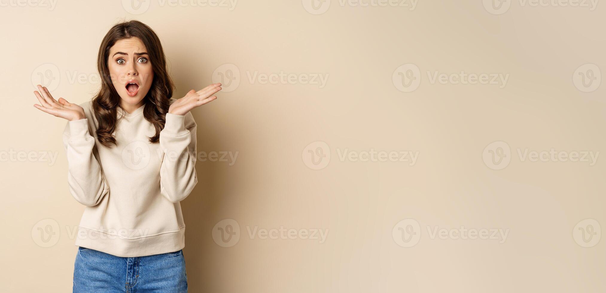 Shocked girl looking startled at camera, drop jaw and spread hands sideways in questioned and stunned face expression photo
