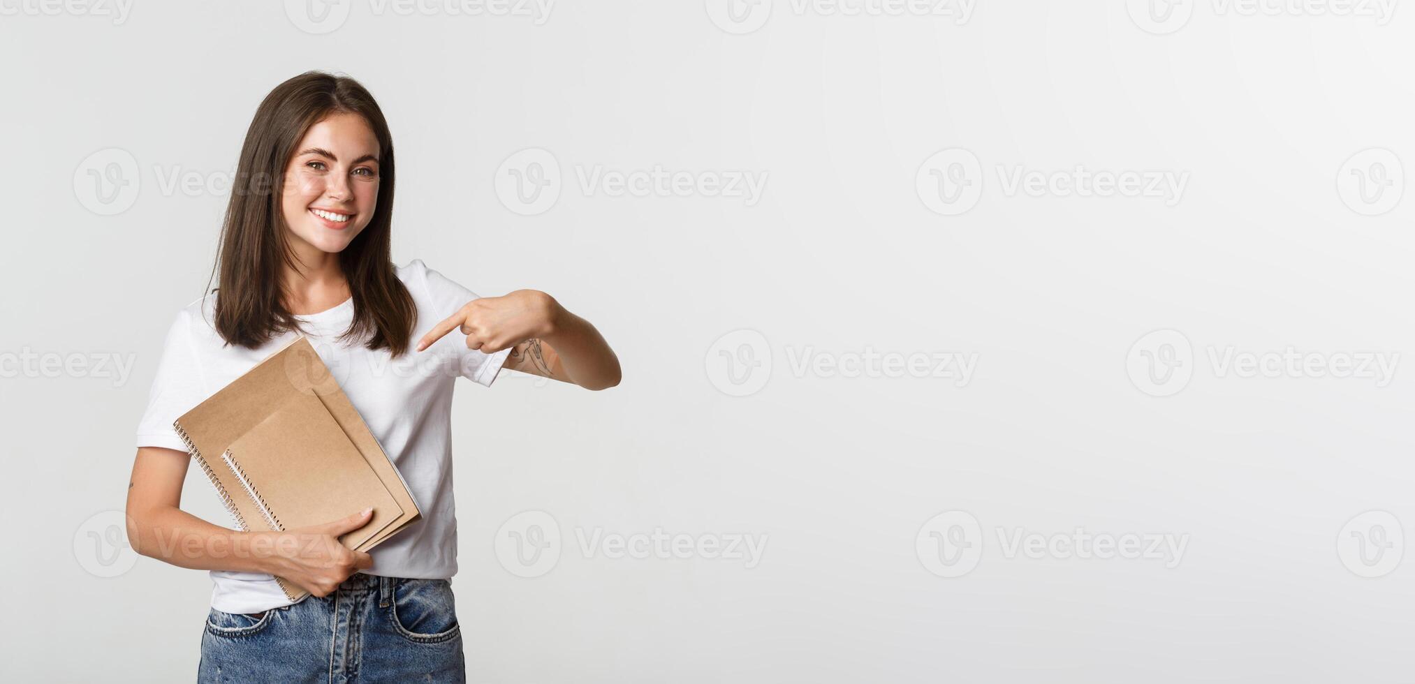 Portrait of smiling brunette girl pointing finger at notebooks, concept of courses or studying photo