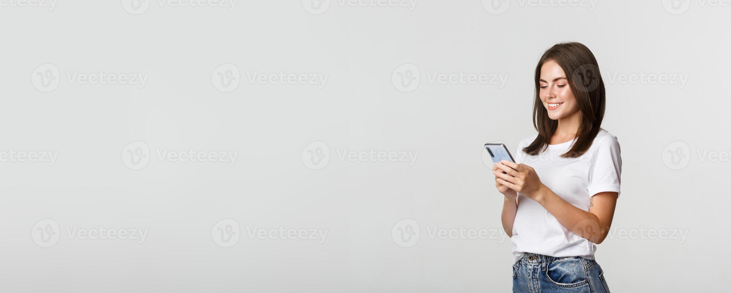 Beautiful smiling girl using mobile phone, looking at smartphone pleased photo