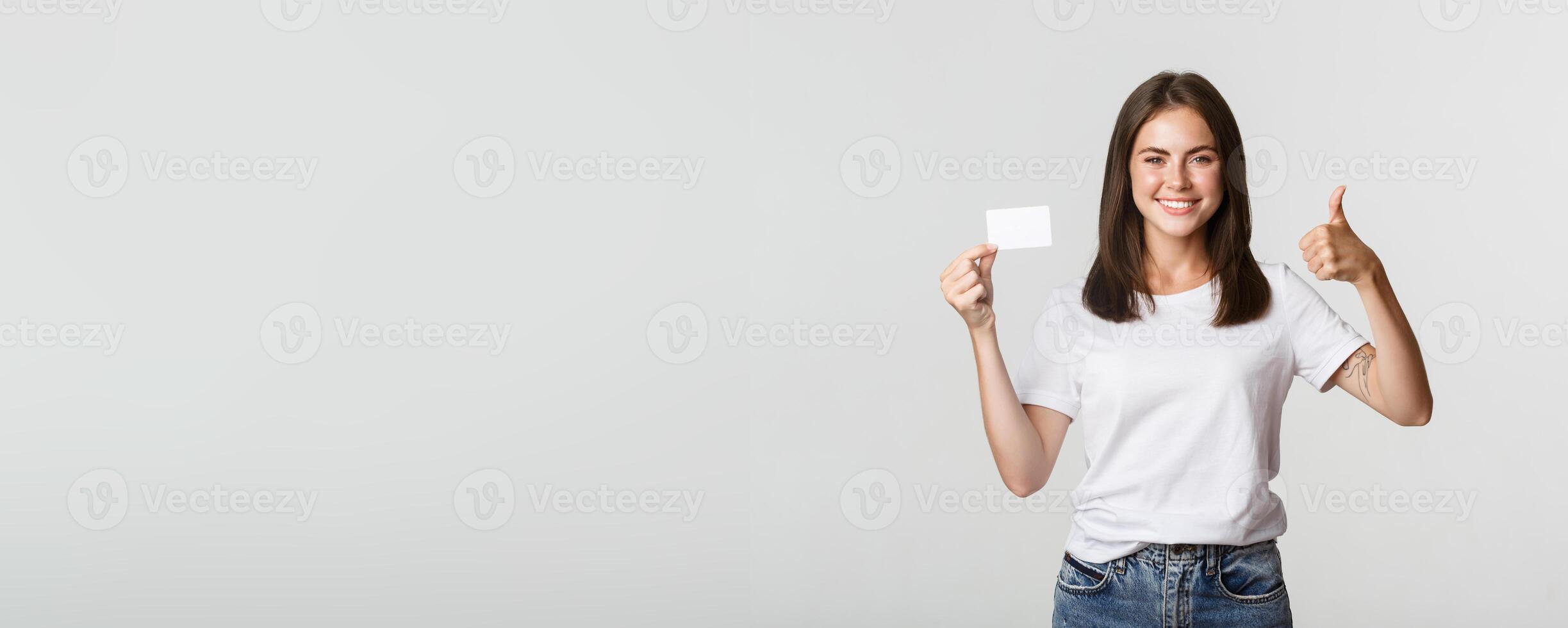 Satisfied attractive girl showing credit card and thumbs-up photo