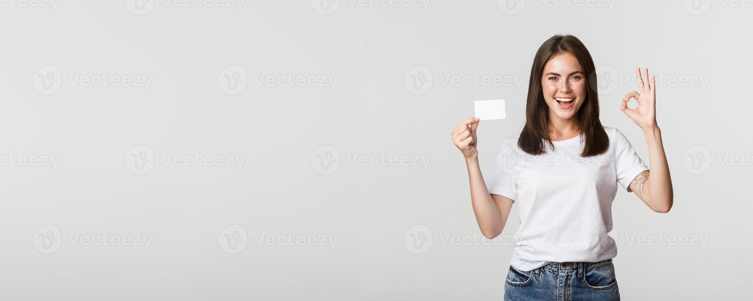 Satisfied attractive brunette girl showing credit card and okay gesture, recommend bank photo