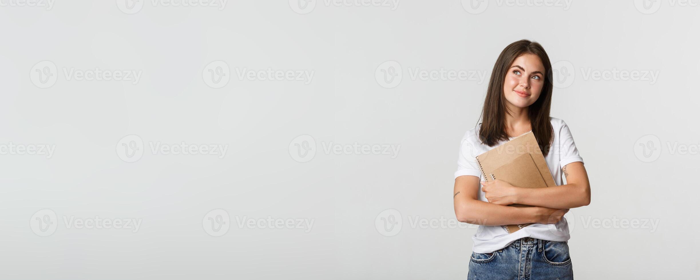 Portrait of smiling nostalgic female student looking upper left corner, holding notebooks photo
