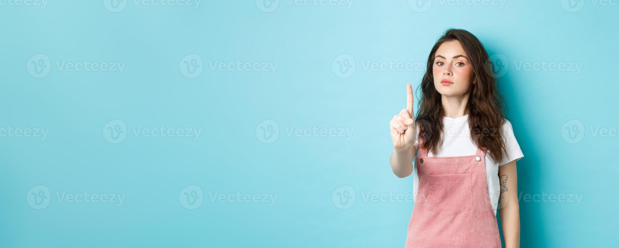 Rule number one. Serious young beautiful girl shaking finger in disapproval, scolding bad decision, make block or taboo gesture, standing against blue background photo