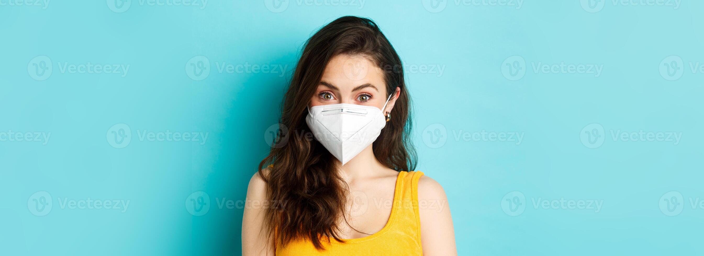 Covid-19, coronavirus and social distancing. Attractive young woman wearing respirator from coronavirus, looking at camera, blue background photo