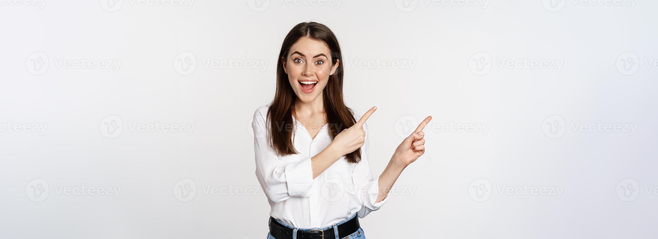 Portrait of enthusiastic smiling woman, female entrepreneur pointing fingers left and showing advertisement, showing announcement, white background photo