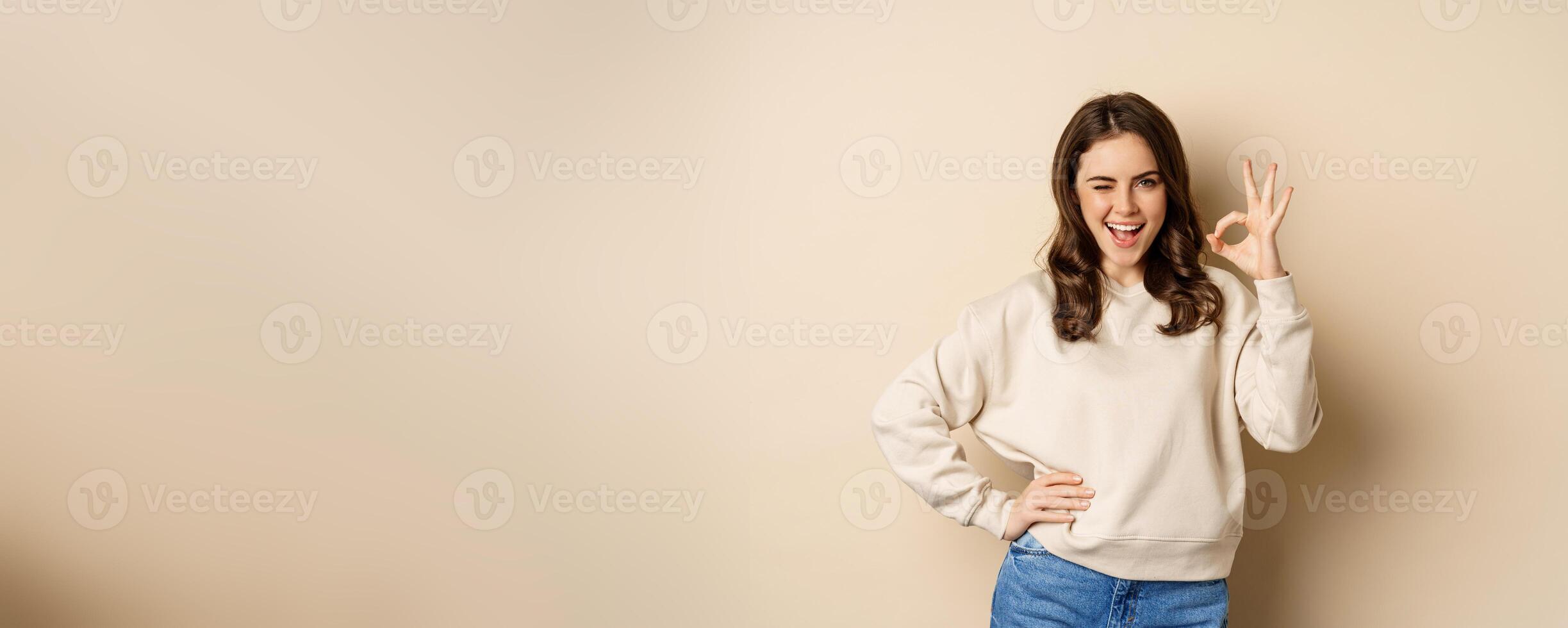 Excellent. Smiling beautiful woman showing okay, ok zero sign, approve smth good, praising and complimenting, beige background photo