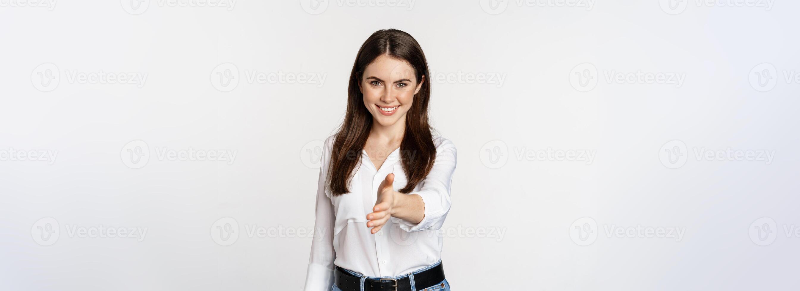 Smiling, friendly corporate woman extending arm for handshake, shaking hand, greeting business partner, standing over white background photo