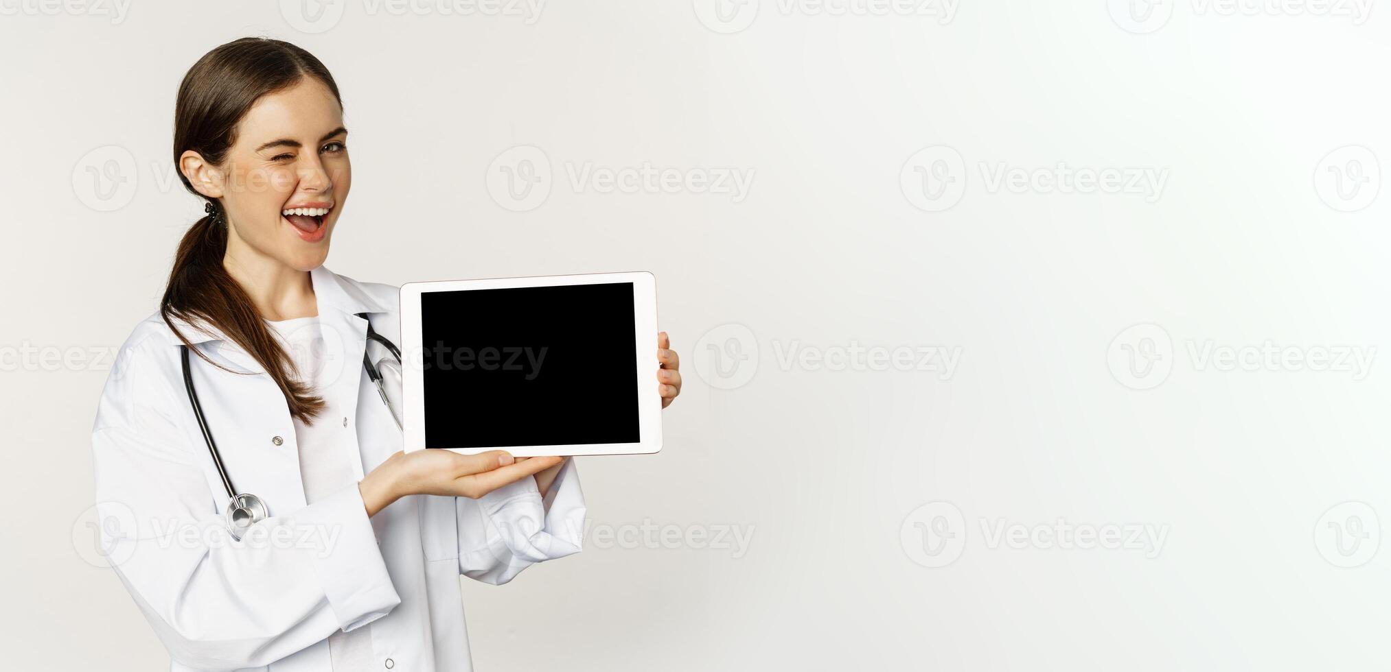 Image of woman doctor, female healthcare worker showing online medical website, digital tablet screen and smiling, standing in white coat over white background photo
