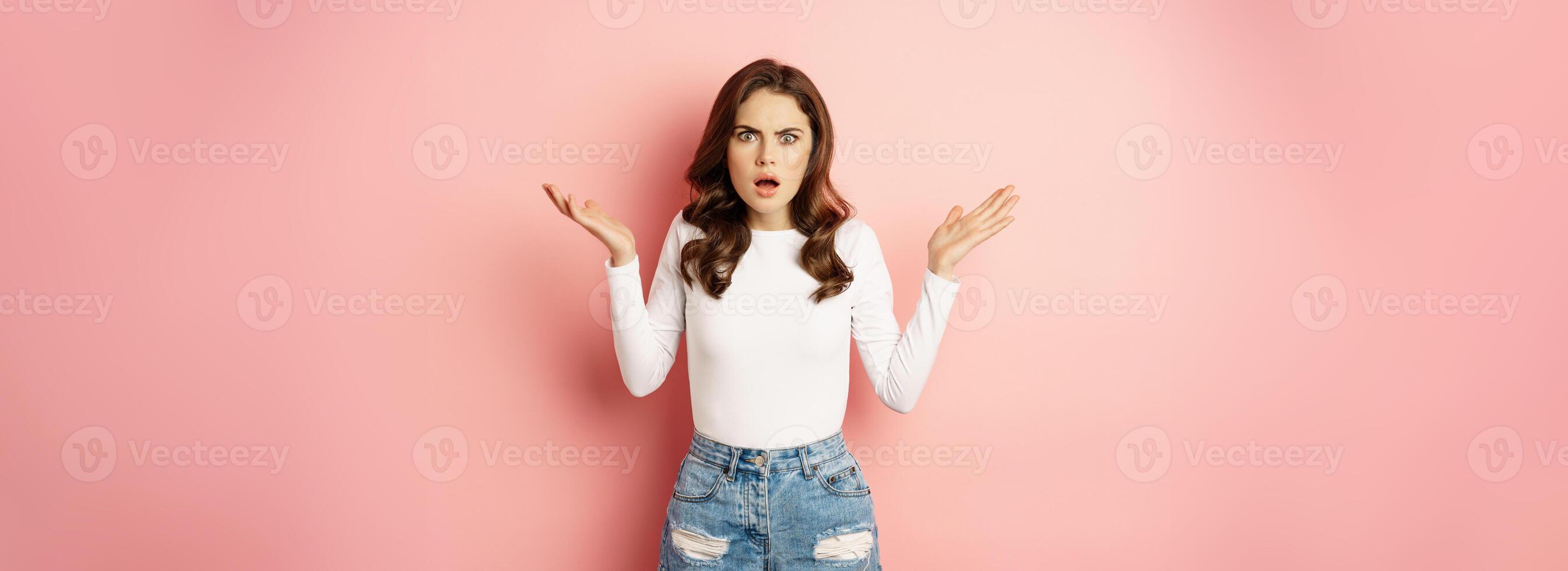 Frustrated young woman, staring at camera, oh my gosh face, frowning shocked, standing against pink background photo