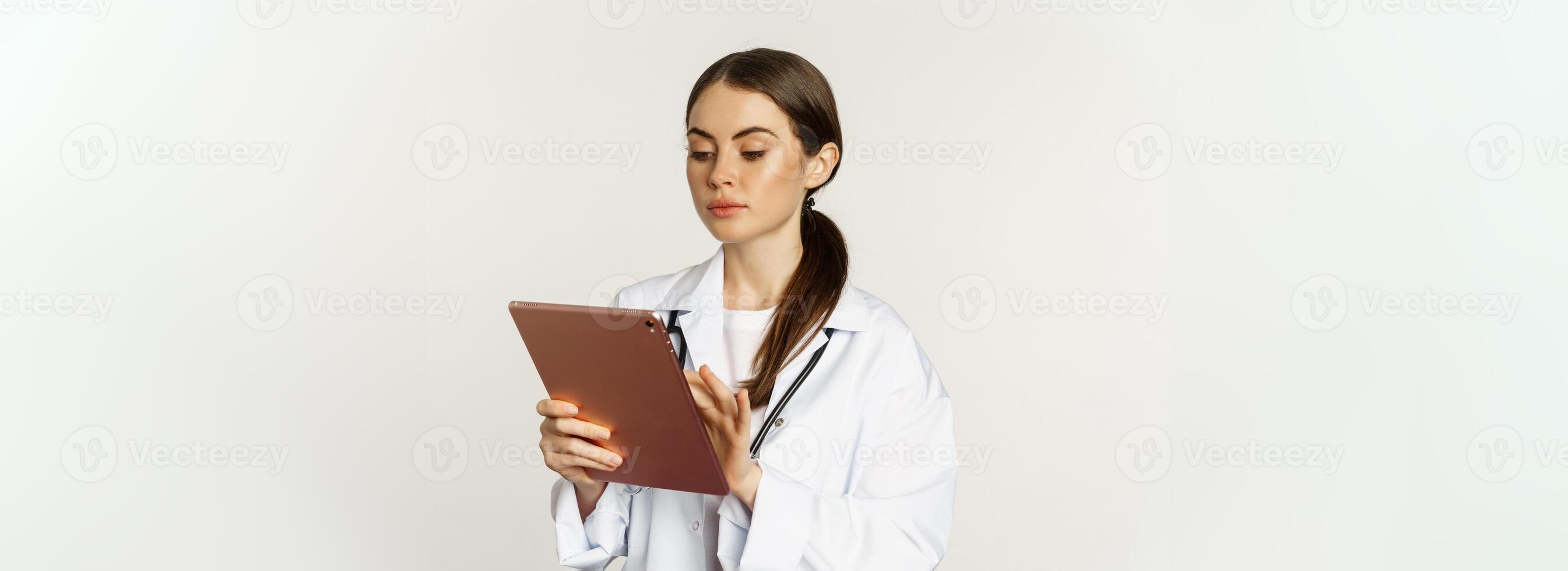 Doctor in white coat using digital tablet, reading medical data on gadget, working in hospital, standing over white background photo