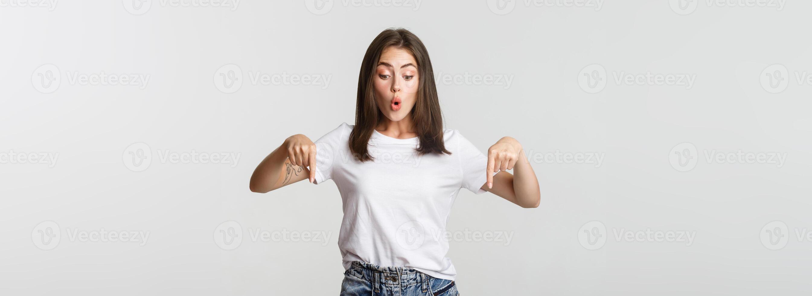 Intrigued attractive girl looking amused and pointing fingers down at logo photo