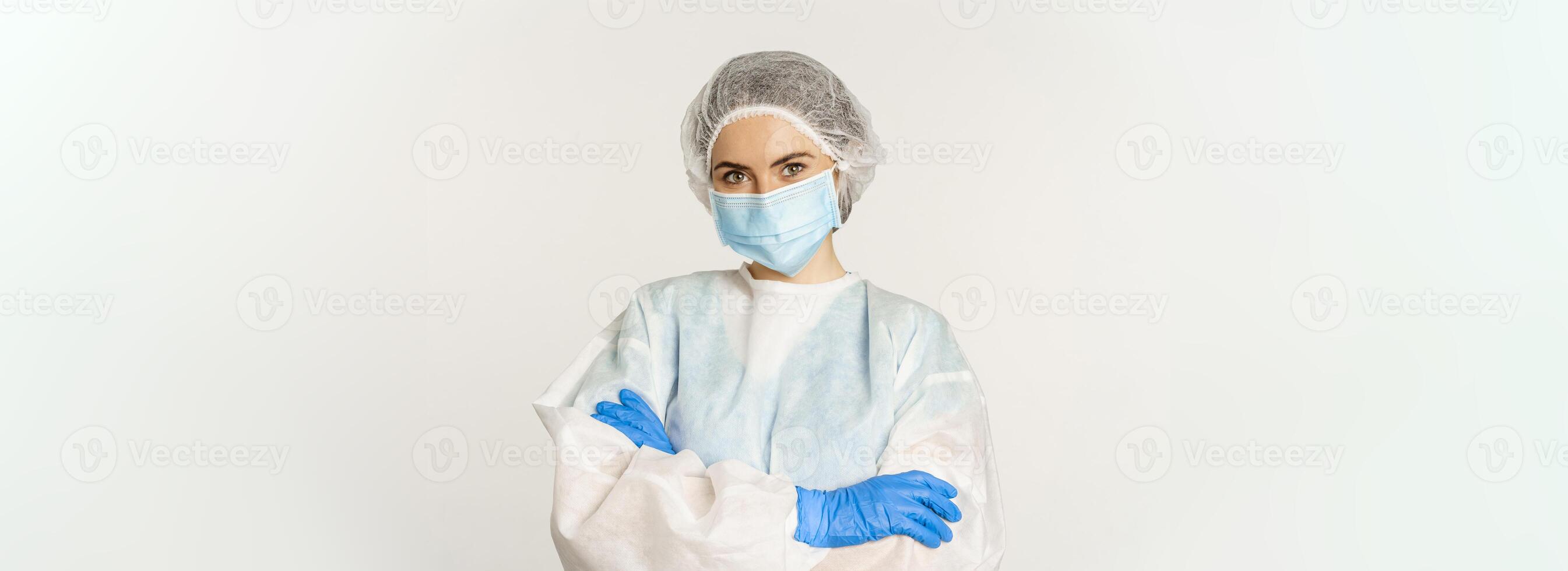 Portrait of doctor, female nurse in personal protective equipment, looking confident and professional, standing over white background photo