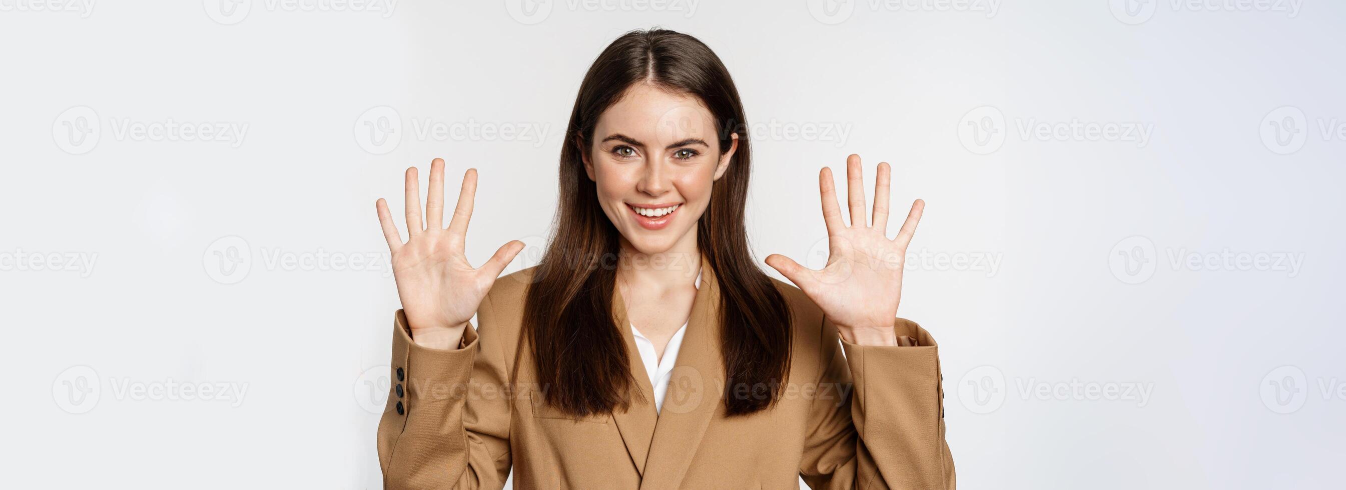Portrait of corporate woman, saleswoman showing number ten fingers and smiling, standing in suit over white background photo