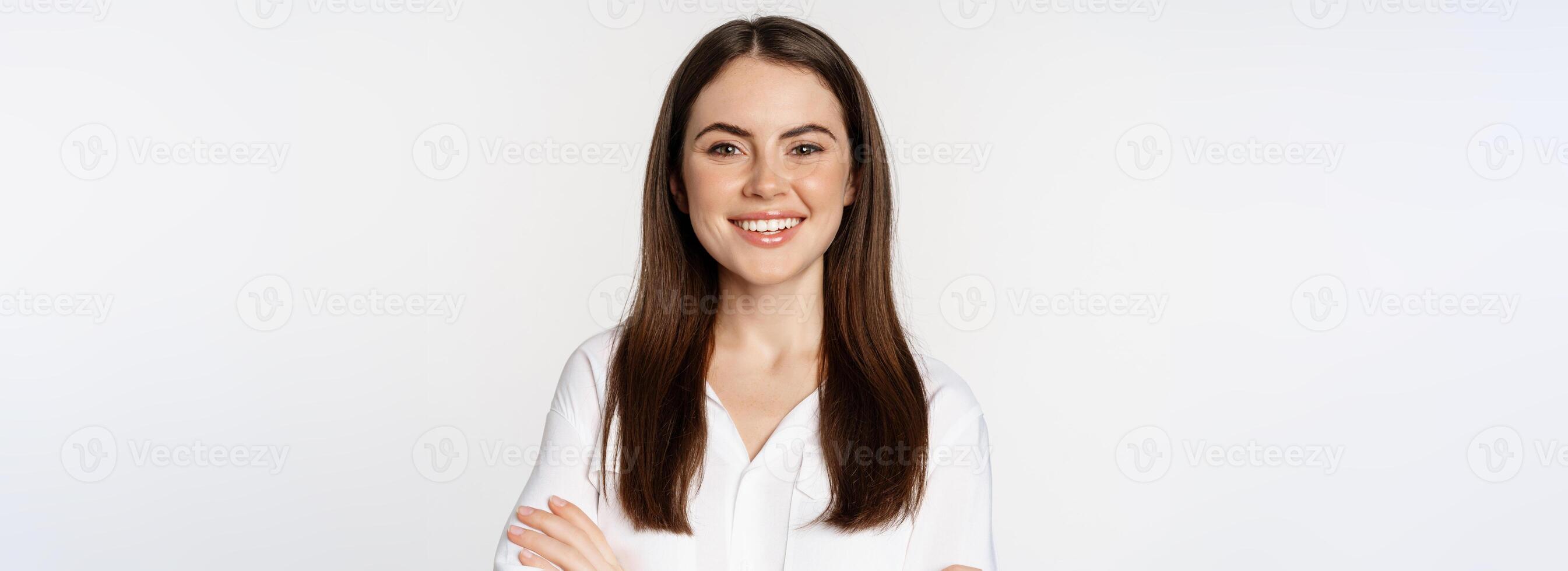 Close up of confident corporate woman, professional entrepreneur smiling, cross arms on chest and smiling enthusiastic, standing over white background photo