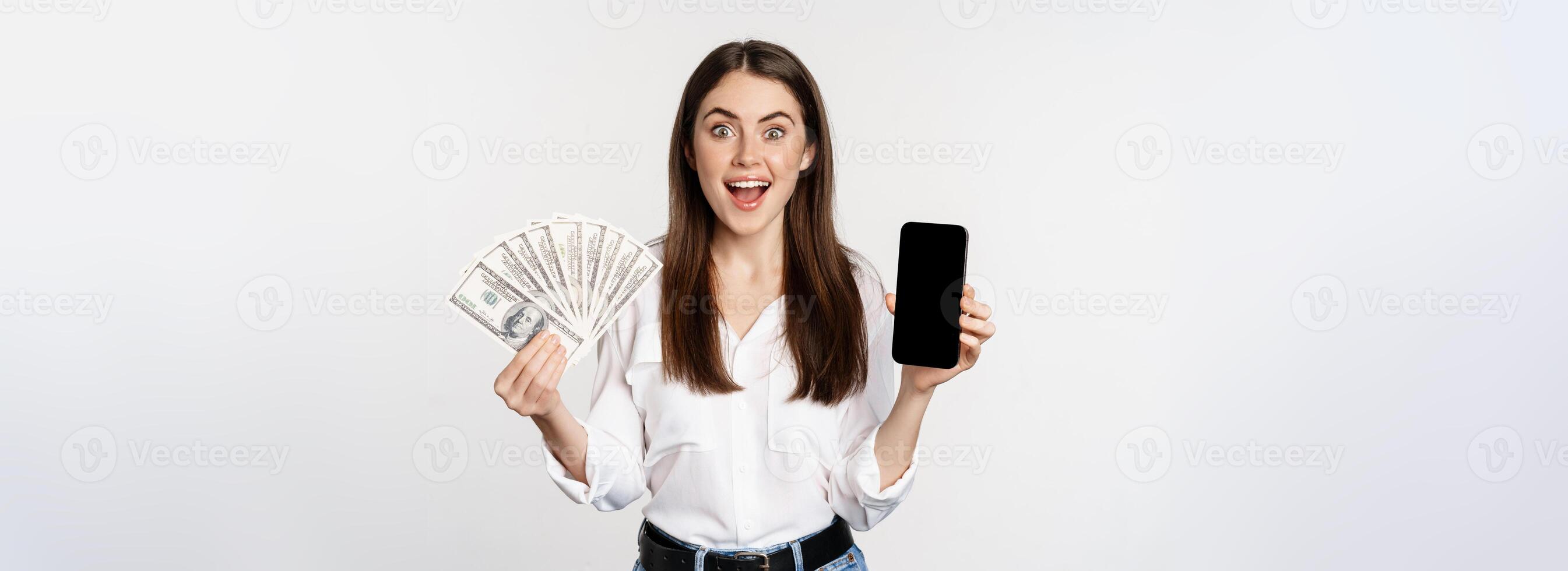Woman showing mobile phone screen and cash, money, concept of microcredit and bank loans, standing over white background photo