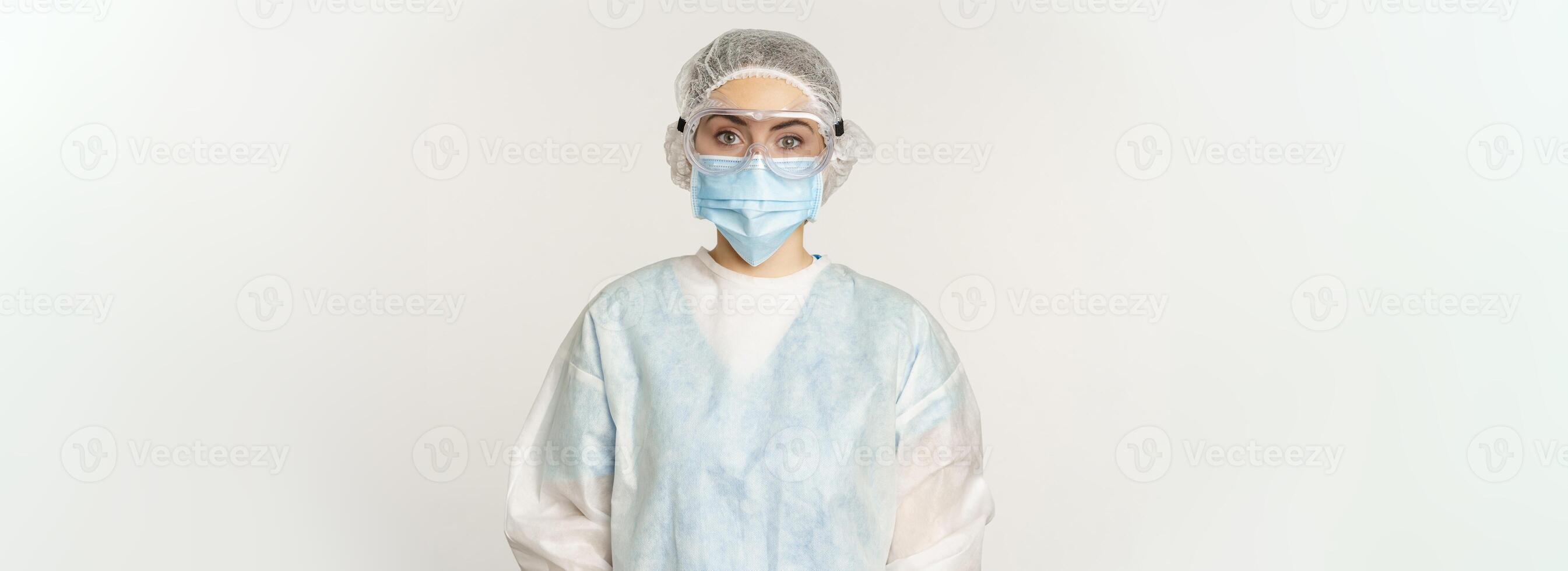 Portrait of doctor, female nurse in personal protective equipment, looking confident and professional, standing over white background photo