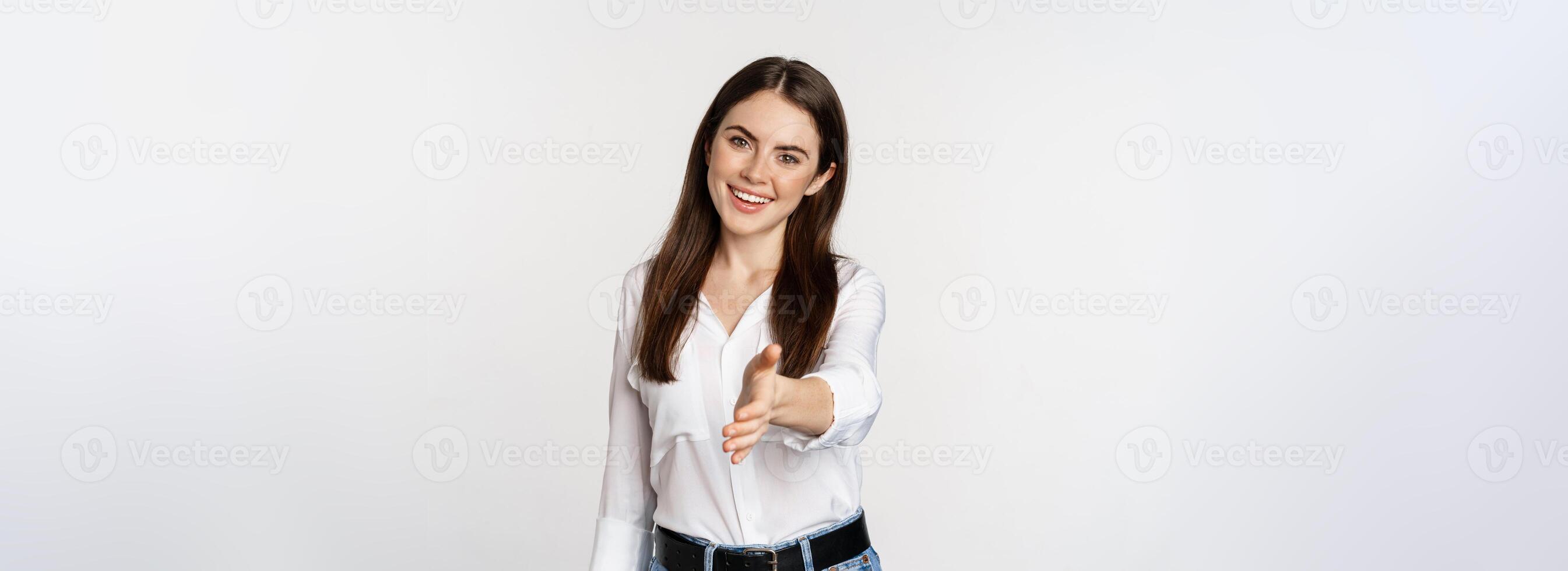Smiling, friendly corporate woman extending arm for handshake, shaking hand, greeting business partner, standing over white background photo