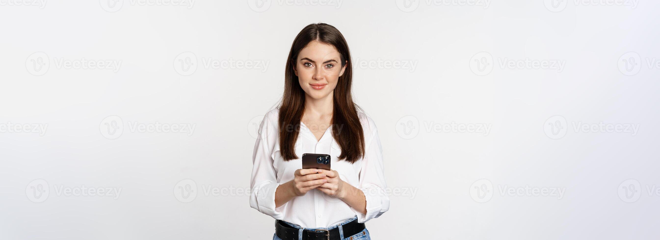 Young woman with smartphone, smiling and looking at camera, using mobile phone app, cellular technology and online shopping concept, white background photo