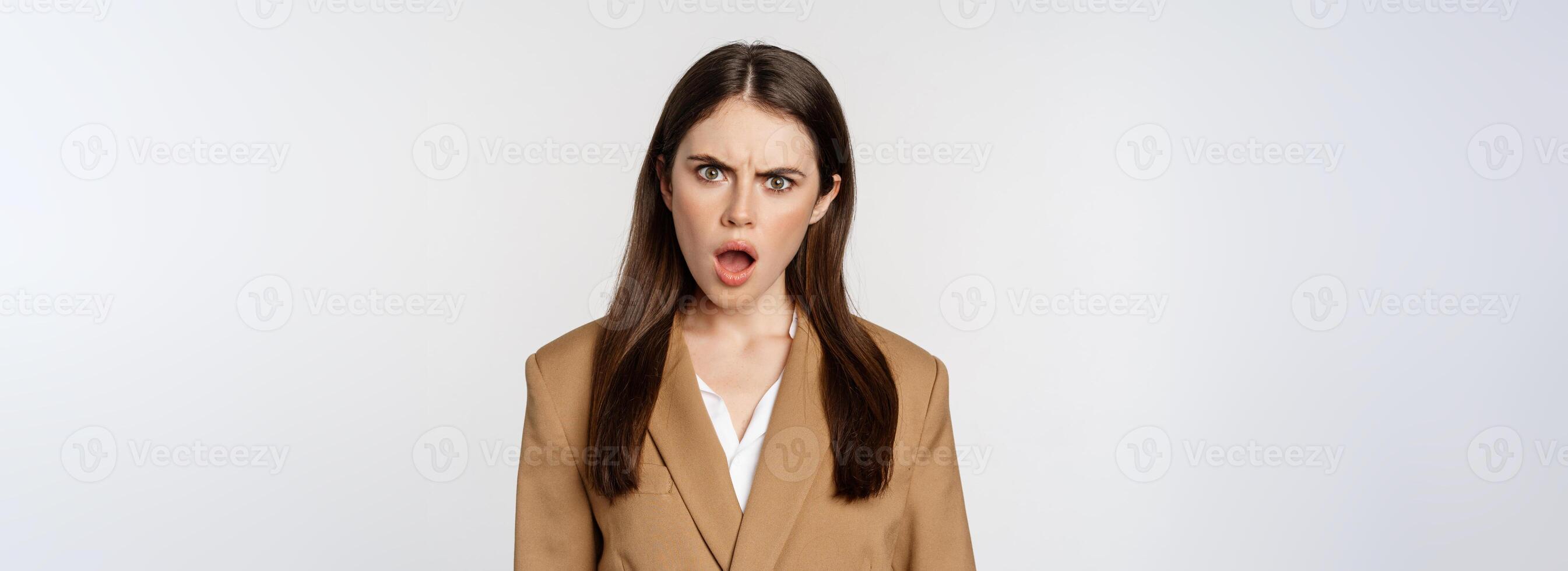 Frustrated, insulated woman in business outfit, staring startled and shocked at camera, standing over white background photo