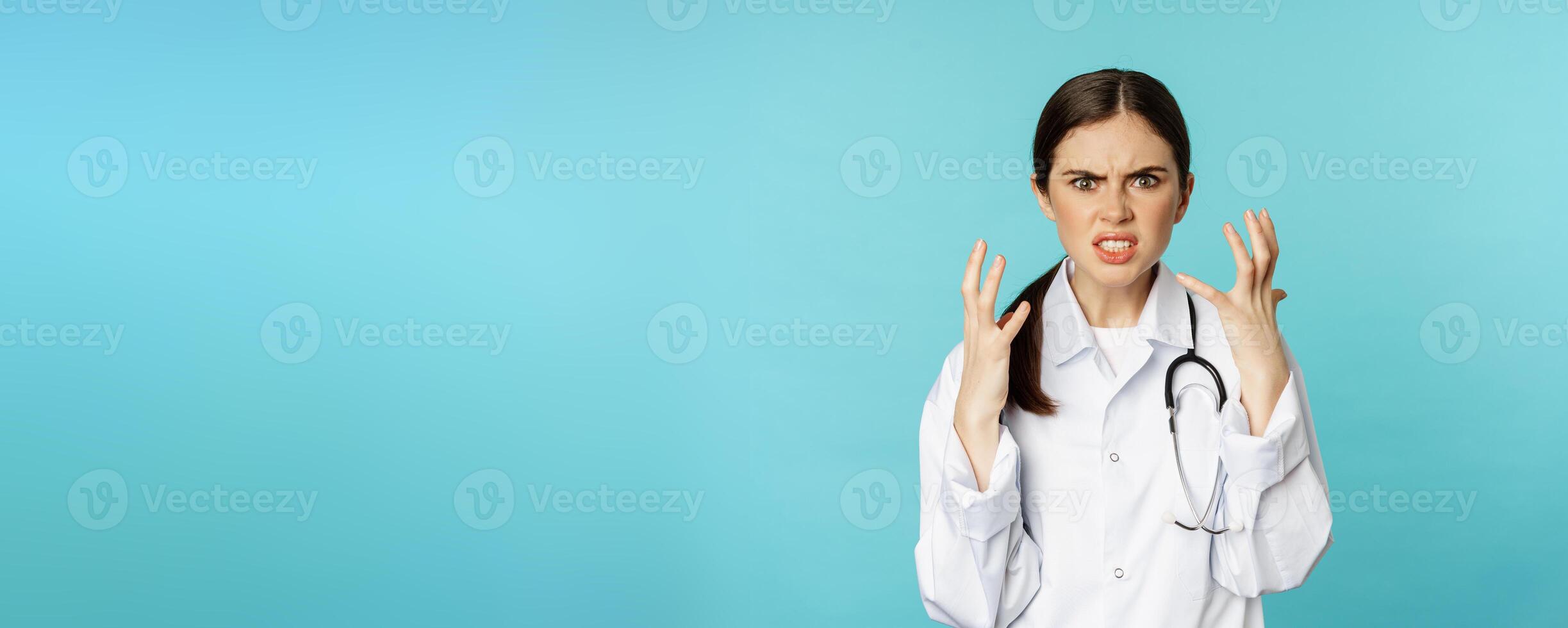 Angry and outraged woman shaking hands, cursing and looking furious, standing annoyed against torquoise background photo