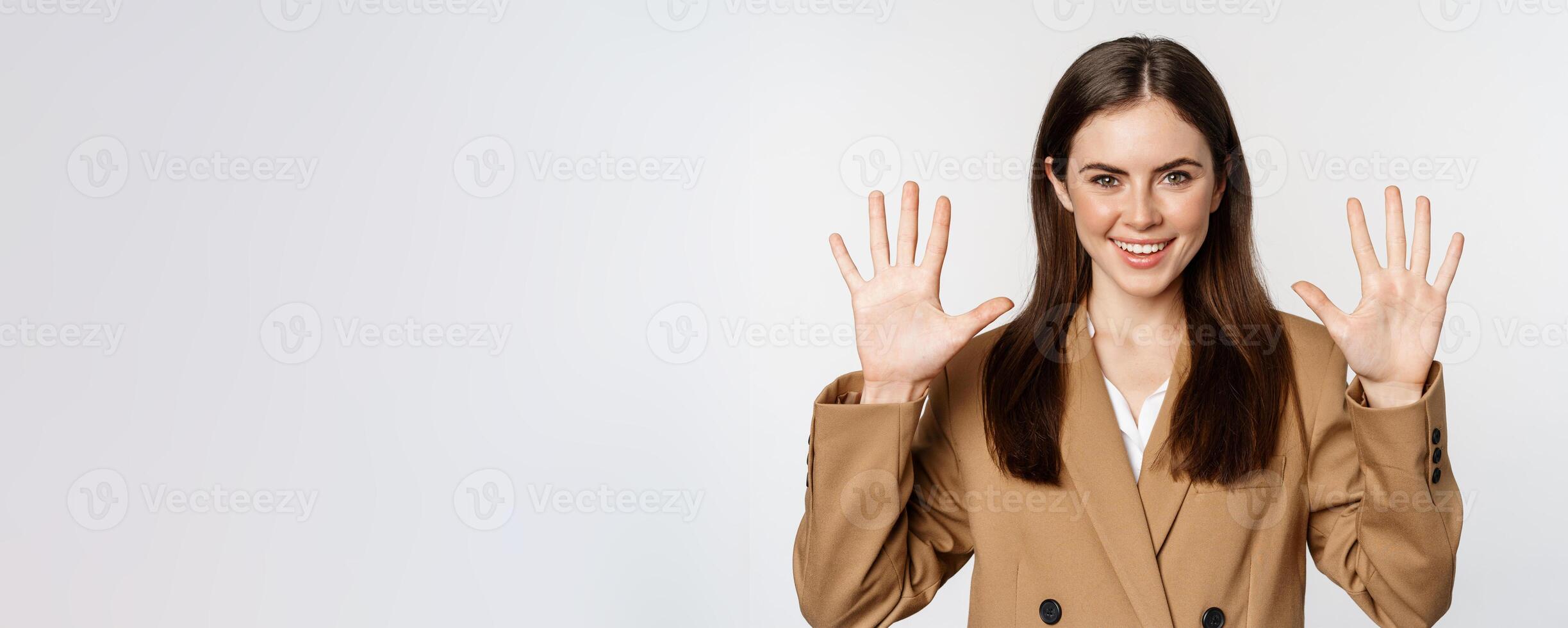 Portrait of corporate woman, saleswoman showing number ten fingers and smiling, standing in suit over white background photo