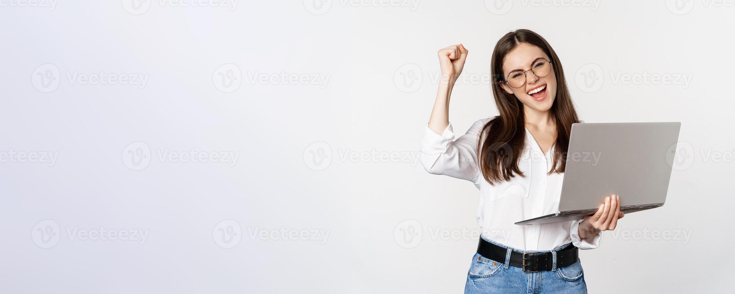 Enthusiastic office woman, businesswoman holding laptop and shouting with joy, celebrating and rejoicing, standing over white background photo