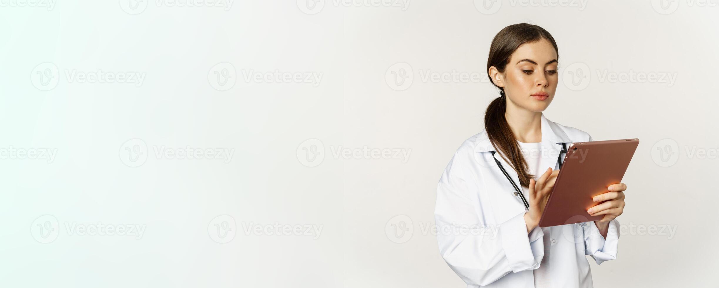 Doctor in white coat using digital tablet, reading medical data on gadget, working in hospital, standing over white background photo