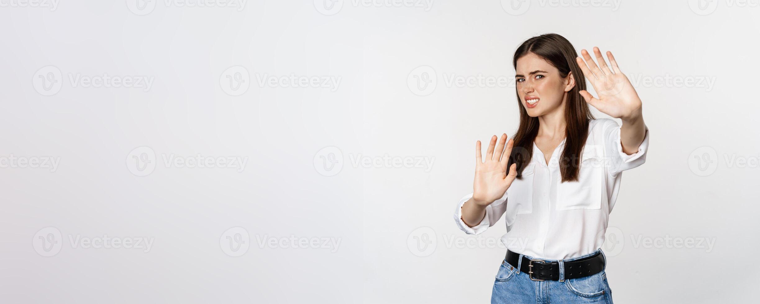 Displeased woman showing stop, rejection gesture, waving hands to decline, refuse of something ugly, standing over white background photo