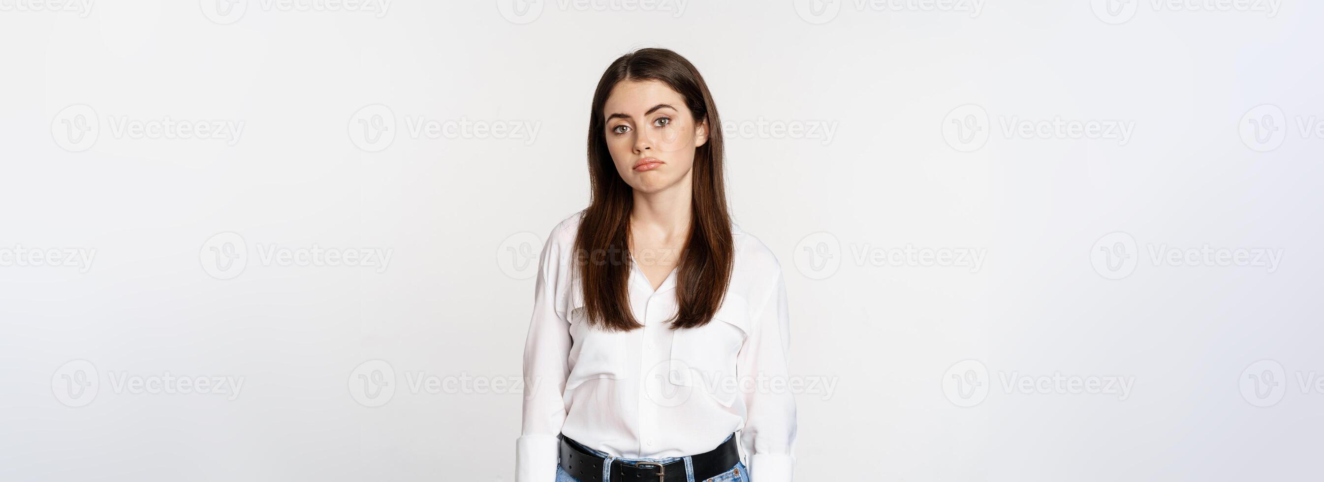 Sad and gloomy woman sulking, looking disappointed and moody, standing upset against white background photo