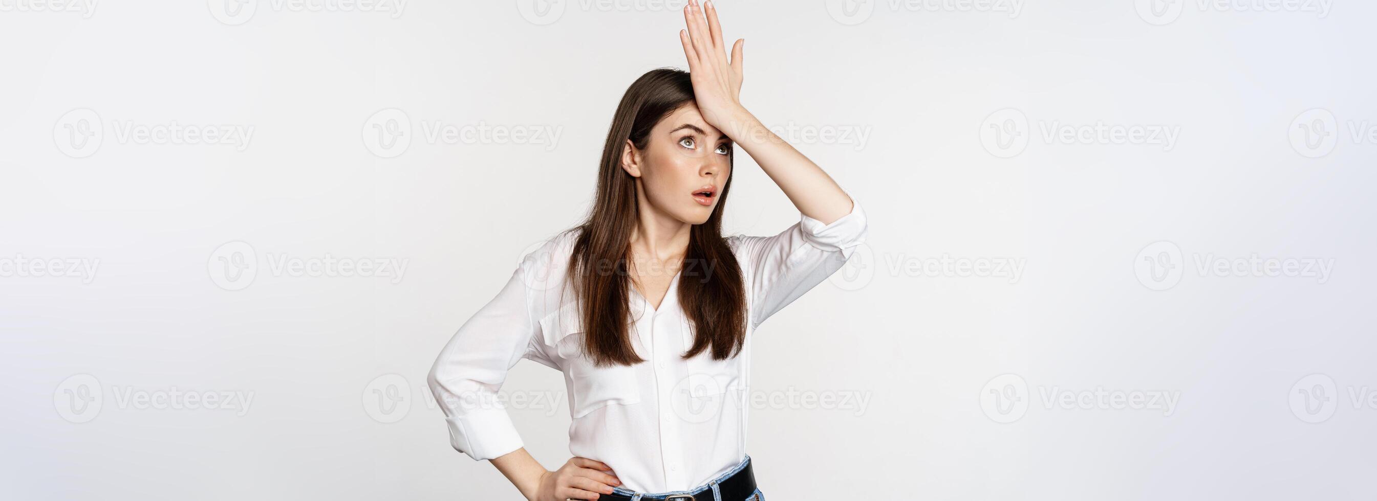 Annoyed young woman facepalm, slap forehead and roll eyes bothered, standing in white shirt and jeans over white background photo