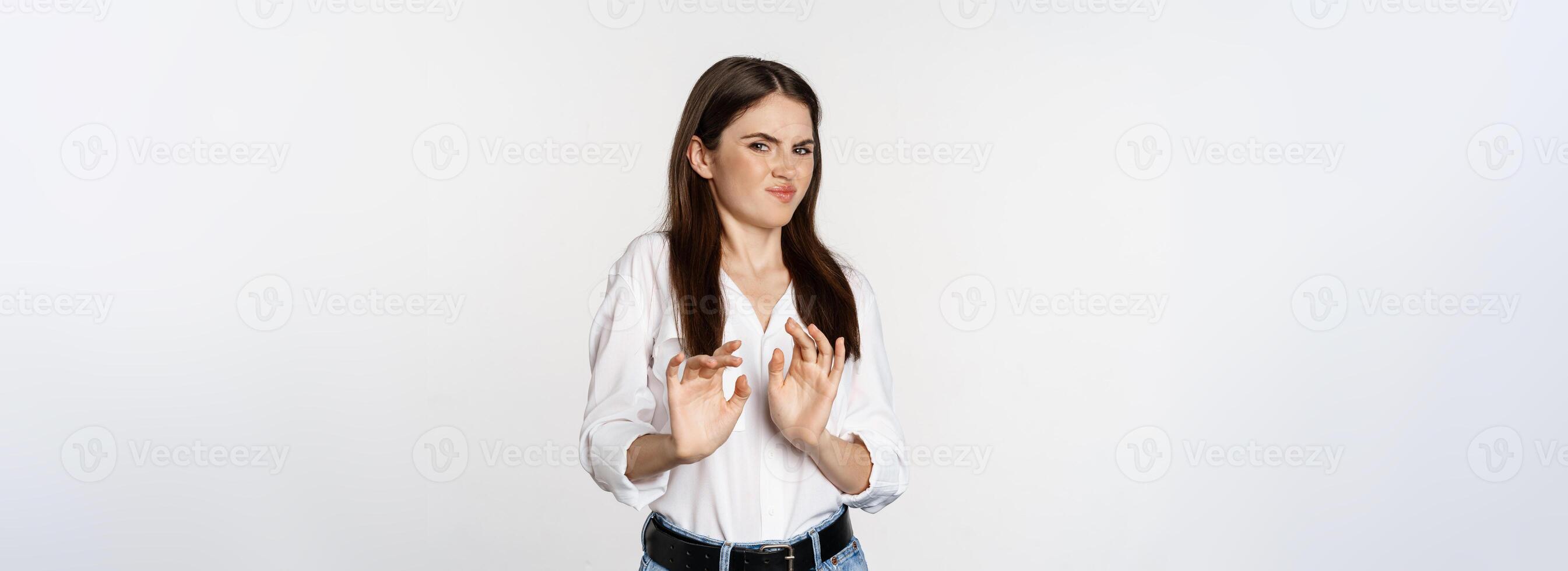 Displeased woman showing stop, rejection gesture, waving hands to decline, refuse of something ugly, standing over white background photo