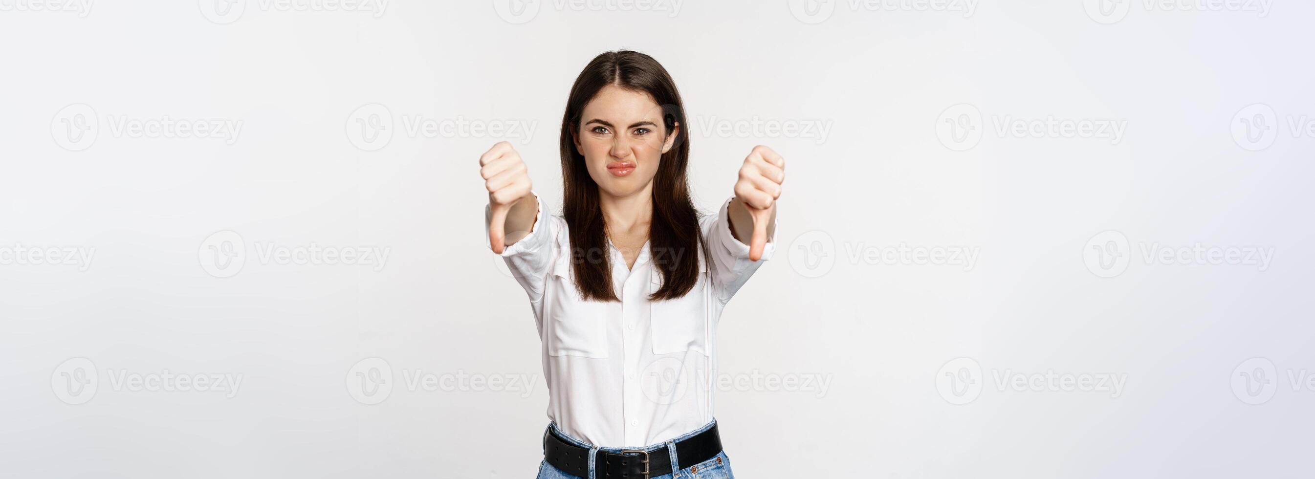 Disappointed adult corporate woman showing thubms down, dislike gesture, negative feedback, complaining and grimacing, white background photo