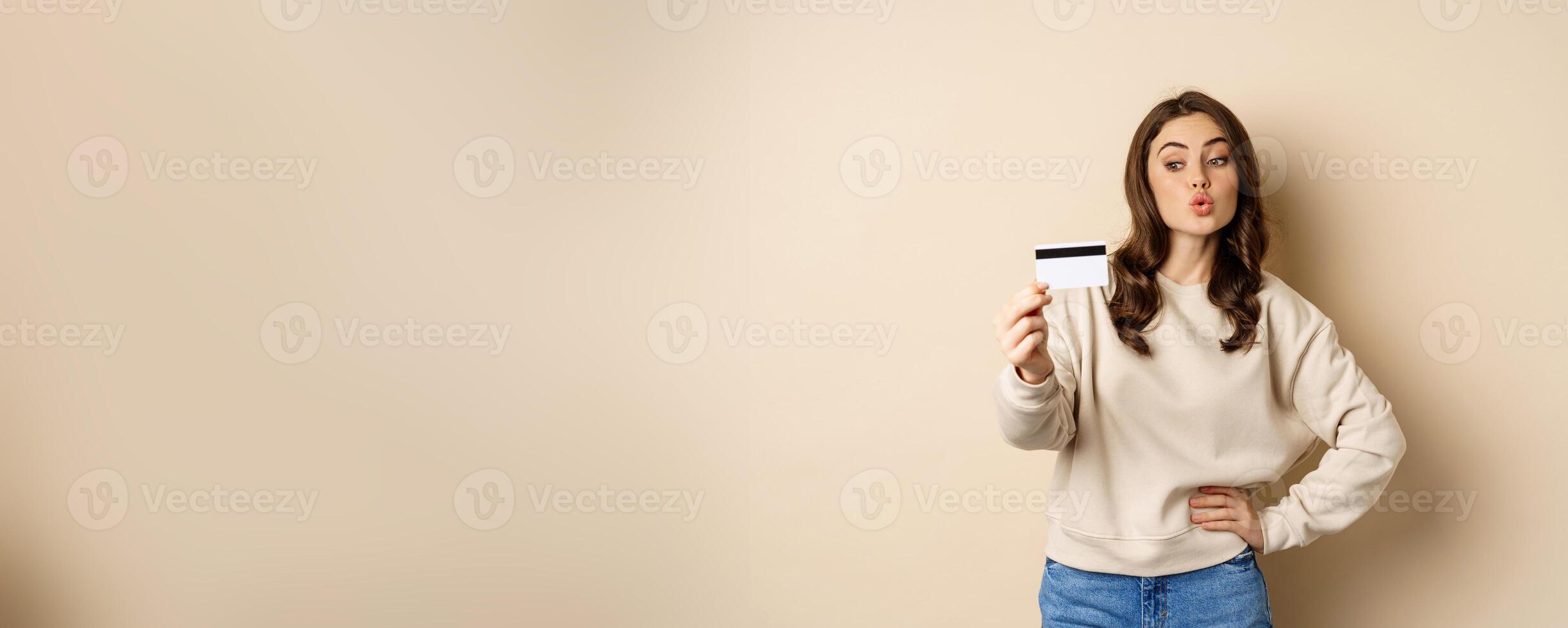 Smiling beautiful woman showing credit card, concept of shopping, contactless payment, standing over beige background photo