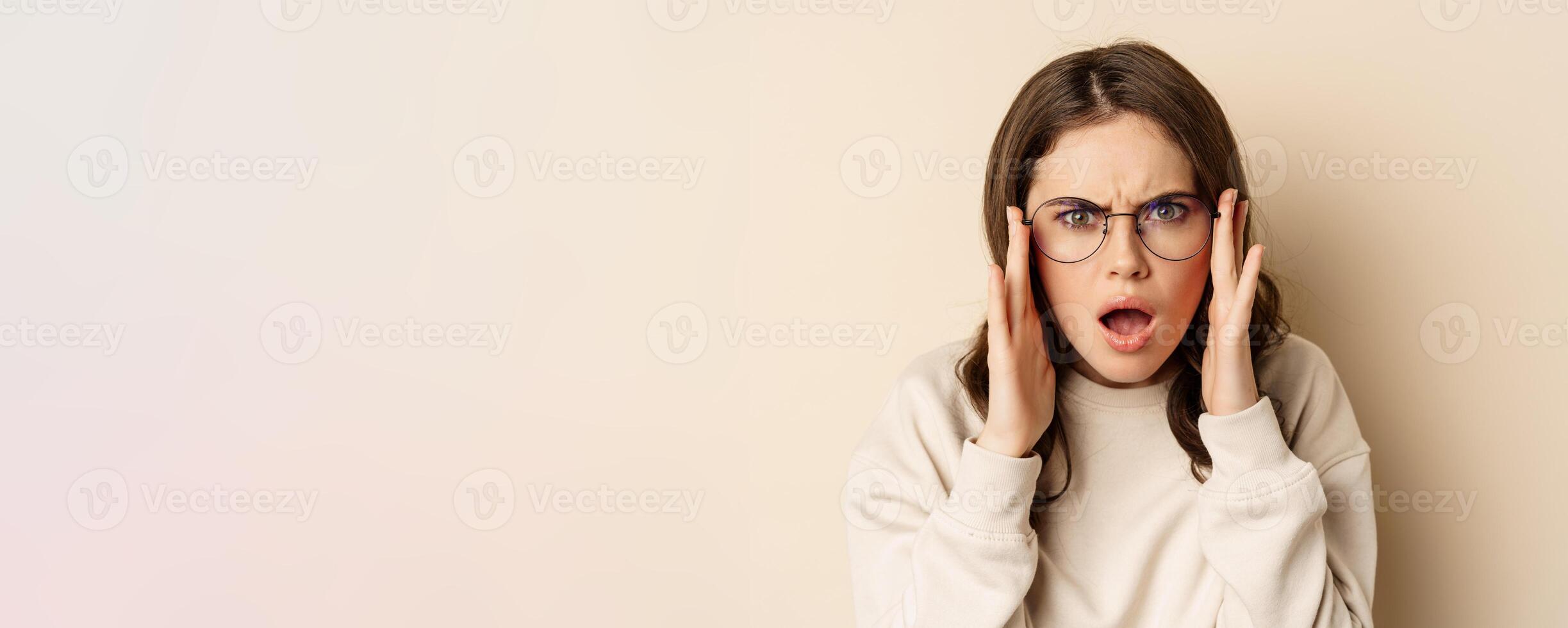 Close up portrait of woman in glasses looking confused and frustrated, cant understand smth strange, standing over beige background photo