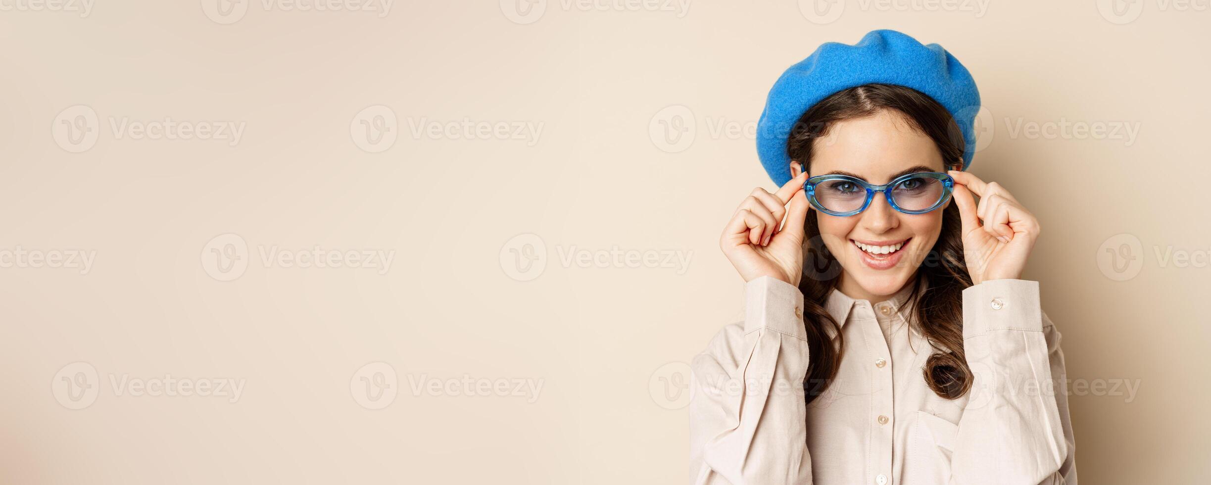 Close up portrait of stylish woman posing in sunglasses, laughing and smiling, wearing trendy outfit, standing over beige background photo