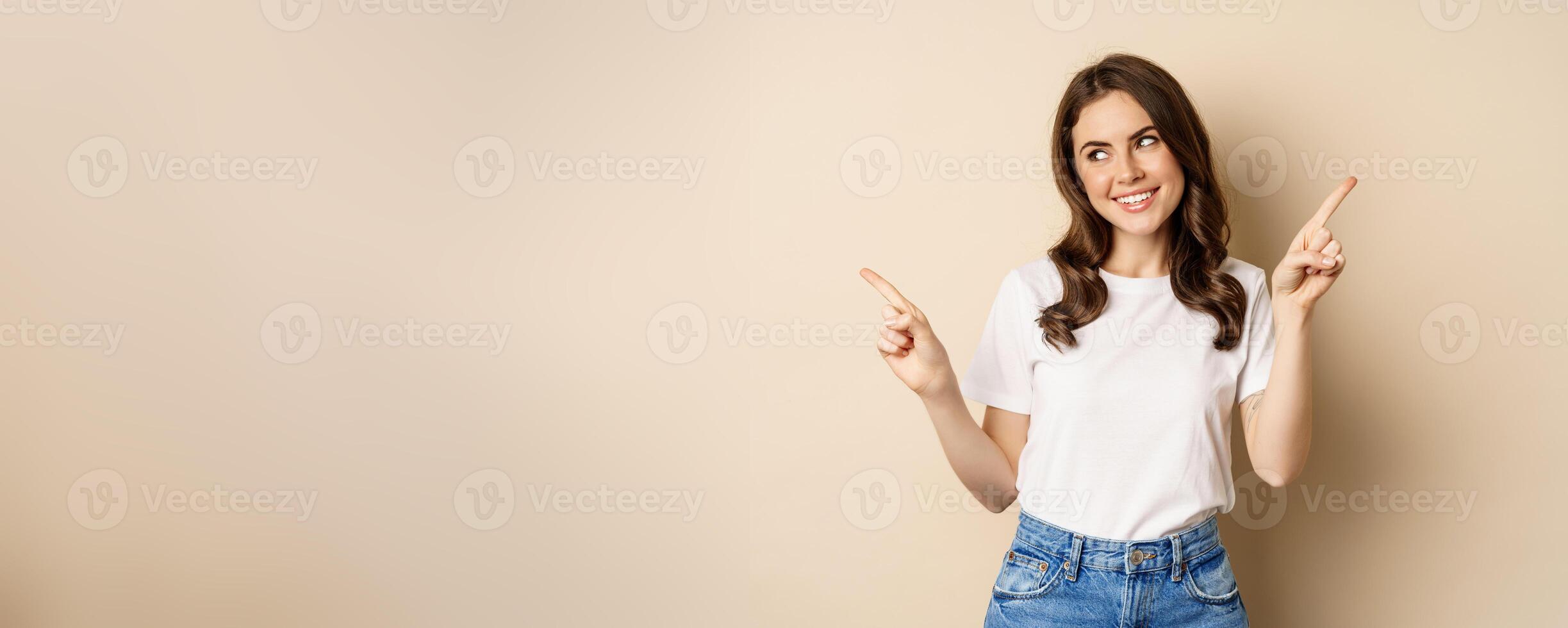 Happy authentic girl smiling, pointing fingers sideways, showing left and right banner, demonstrating promo, standing against beige background photo