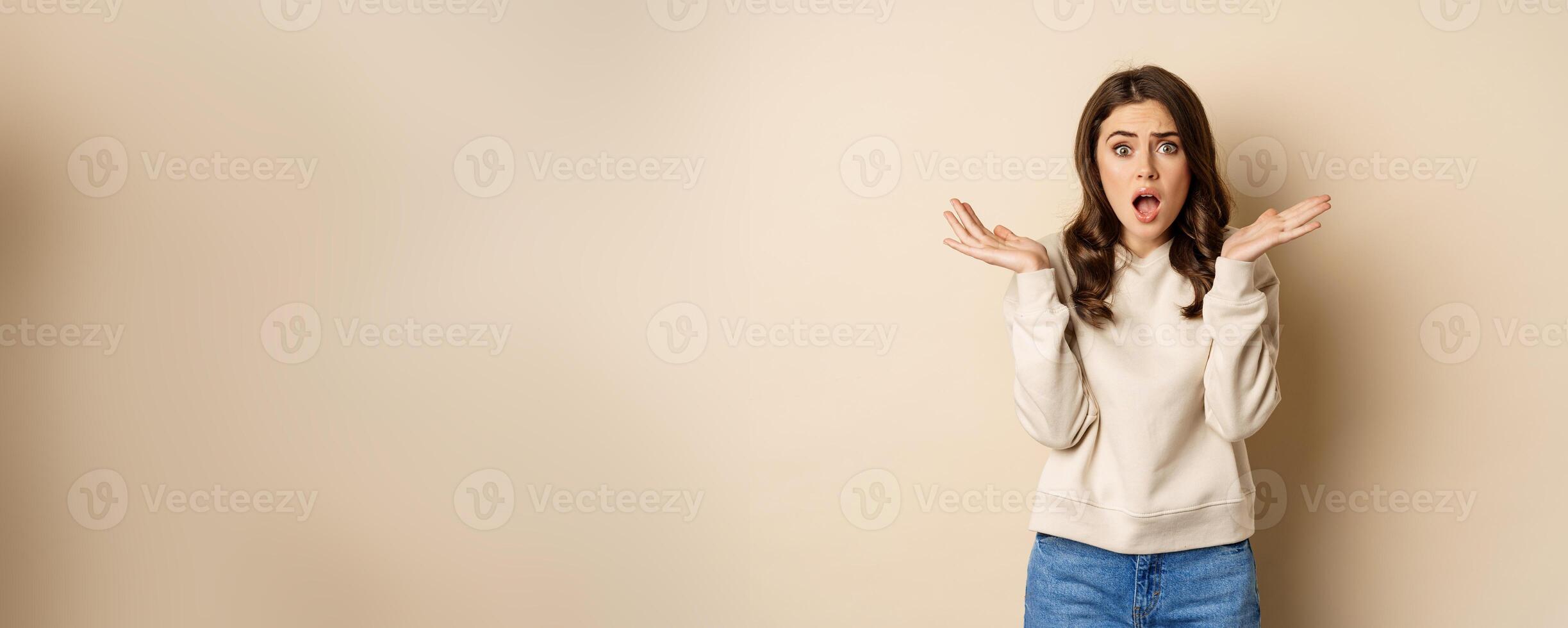 Shocked girl looking startled at camera, drop jaw and spread hands sideways in questioned and stunned face expression photo