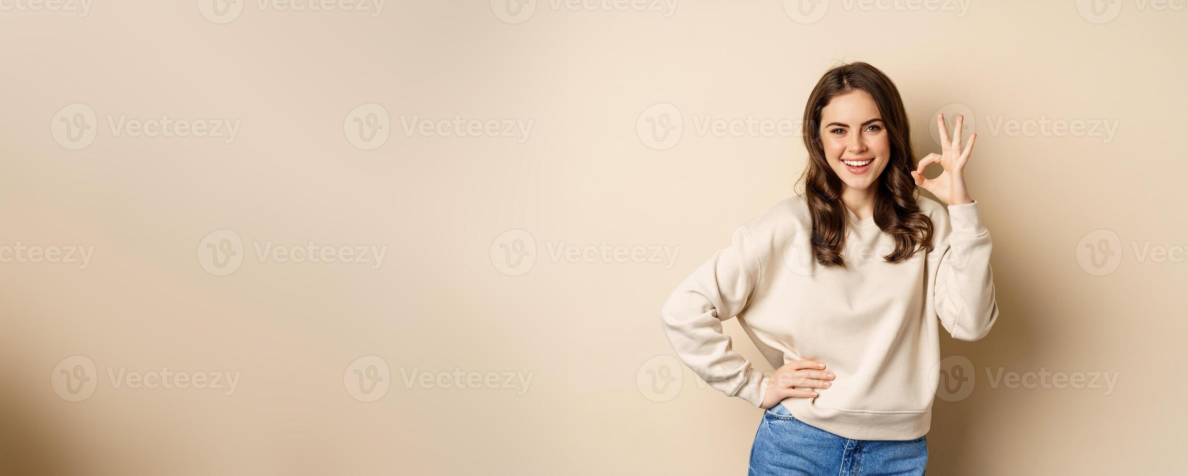 Excellent. Smiling beautiful woman showing okay, ok zero sign, approve smth good, praising and complimenting, beige background photo