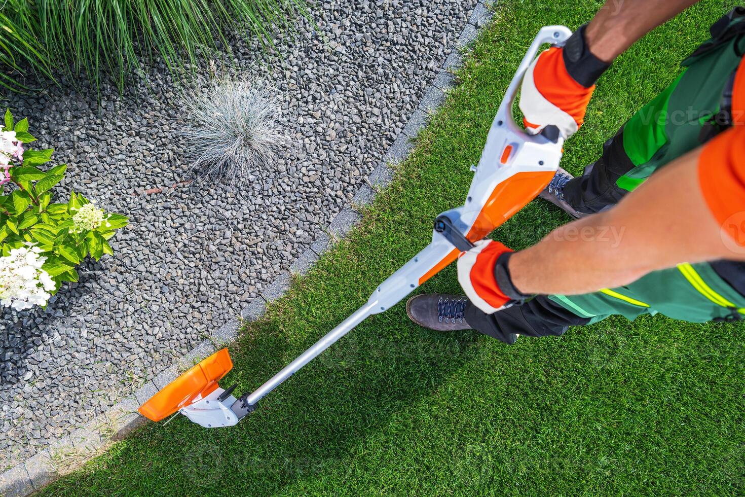 Person Trimming Grass Edges With String Trimmer in a Garden on a Sunny Day photo